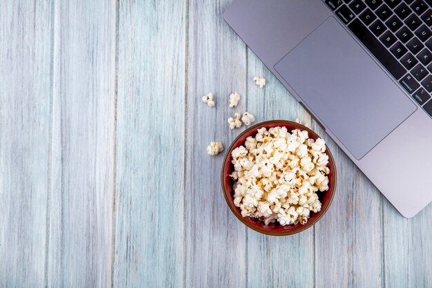 Top view of tasty popcorn on a wooden bowl on grey wooden surface