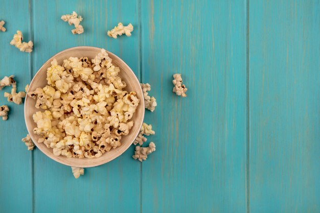 Top view of tasty popcorns on a bowl on a blue wooden table with copy space