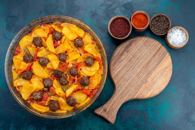 Vista dall'alto di un gustoso pasto di patate con polpette e pomodori sulla superficie blu scuro