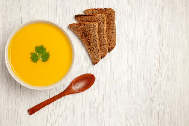 Top view of tasty pumpkin soup cream textured with dark bread loafs on white