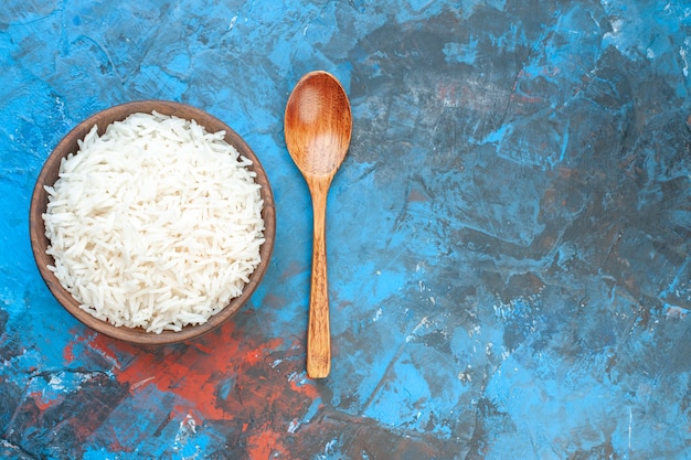 Free photo top view of tasty rice meal in a brown small pot and wooden spoon on the right side on blue table