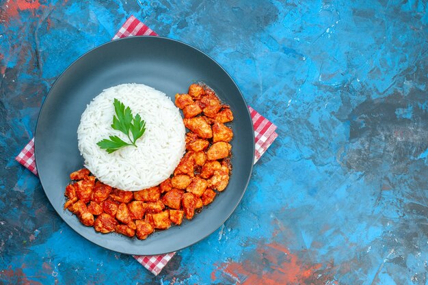 青いテーブルの上の赤いストリップタオルに緑とトマトの鶏肉とおいしいご飯の上面図