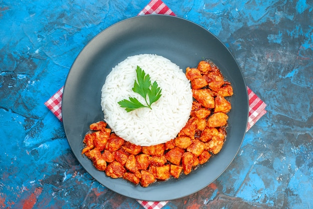 Top view of tasty rice meal with green and tomato chicken on red stripped towel on blue table