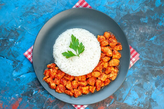 파란색 테이블에 빨간색 벗겨진 수건에 녹색 및 토마토 닭고기와 함께 맛있는 쌀 식사의 상위 뷰