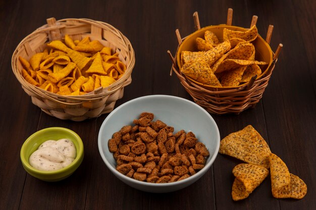 Top view of tasty rye rusks on a bowl with spicy chips on a bucket with sauce on a bowl on a wooden table