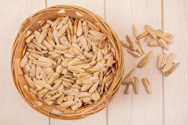 Top view of tasty salty white sunflower seeds on a bucket with seeds isolated on a beige wooden table