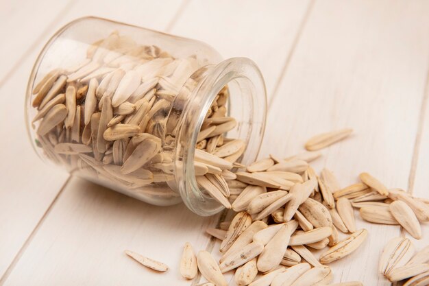 Top view of tasty salty white sunflower seeds falling out of a glass jar on a beige wooden table