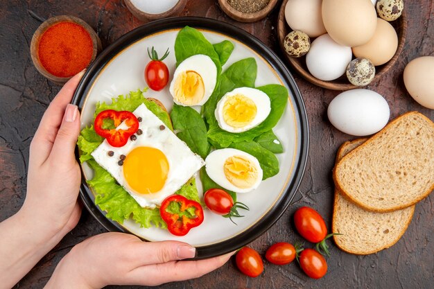 어두운 탁자에 달걀 조미료와 토마토가 있는 맛있는 샌드위치