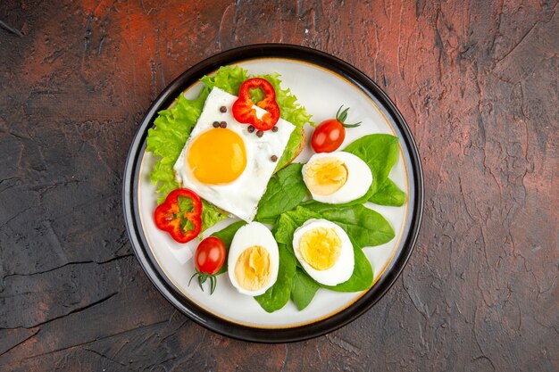 Top view tasty sandwich with scrambled and boiled eggs and salad inside plate on dark table