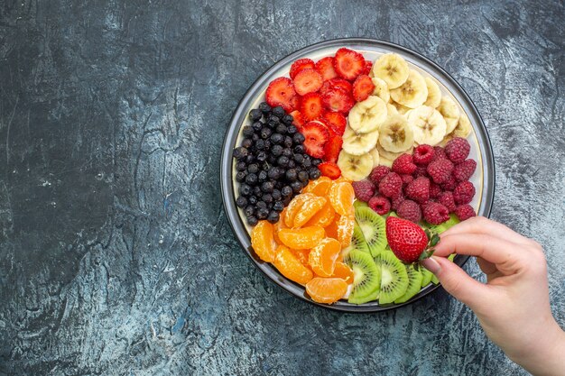 Вид сверху вкусные нарезанные фрукты внутри тарелки на сером фоне