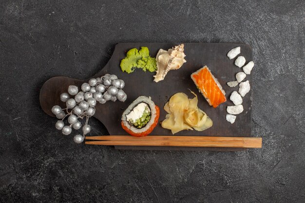 Vista dall'alto di involtini di pesce a fette di pasto gustoso sushi con wassabi e bastoncini sul muro grigio
