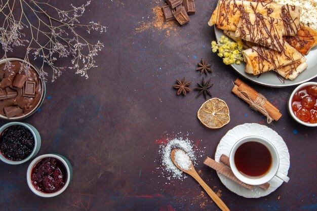 Top view tasty sweet pastries with cup of tea and jam on dark background pastry biscuit cake sugar sweet tea