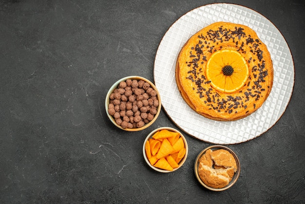 Вид сверху вкусный сладкий пирог с дольками апельсина на темно-сером столе сладкий пирог десертный чай бисквитный торт сахар