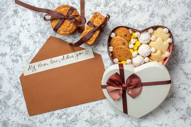 Вид сверху вкусные сладости, печенье, печенье и конфеты внутри коробки в форме сердца на белом фоне, сахарный чай, сладкий вкусный торт