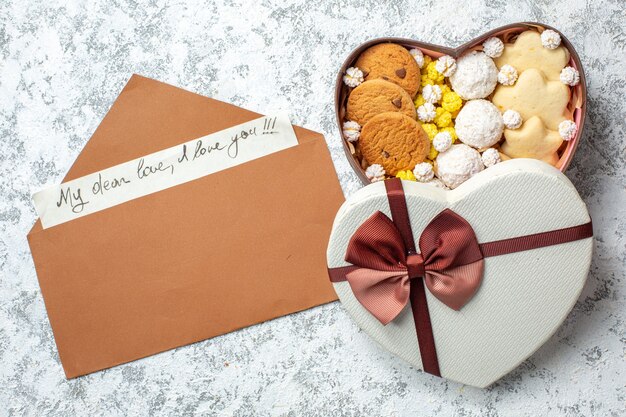 Top view tasty sweets biscuits cookies and candies inside heart shaped box on a white surface sugar pie tea sweet yummy cake