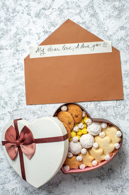 Top view tasty sweets biscuits cookies and candies inside heart shaped box on white surface sugar pie tea sweet yummy cake