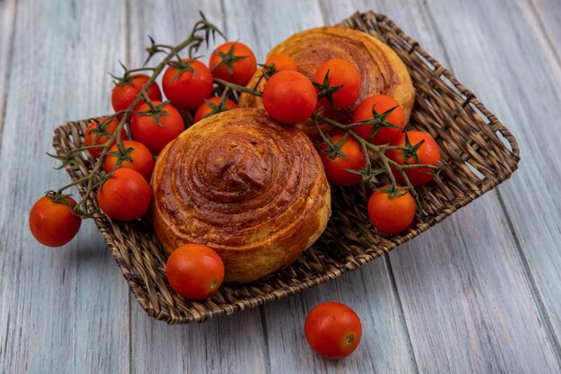 Вид сверху вкусной традиционной азербайджанской выпечки гогаль на плетеном подносе с виноградными помидорами на сером деревянном фоне