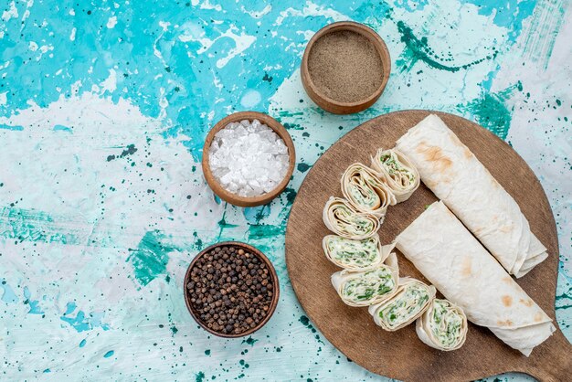 Top view tasty vegetable rolls whole and sliced with greens and seasonings on the bright-blue background food meal roll vegetable color