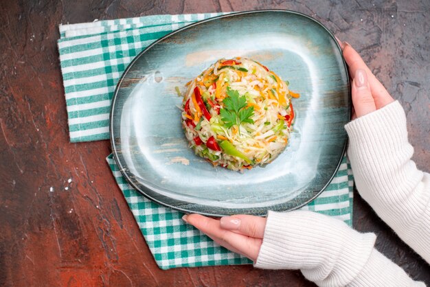 Вид сверху вкусный овощной салат внутри тарелки с женскими руками на темном столе