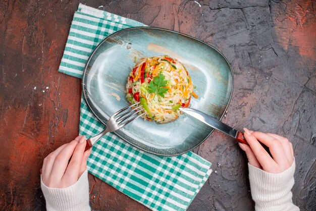 어두운 탁자에 여성의 손이 있는 접시 안에 있는 맛있는 야채 샐러드