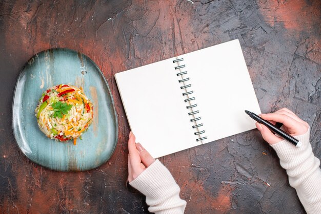 暗いテーブルに描く女性とプレート内のおいしい野菜サラダの上面図