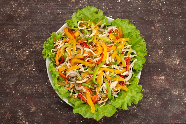 Вид сверху вкусный овощной салат с нарезанными овощами и зеленым салатом внутри тарелки на коричневом, овощной салат еда еда