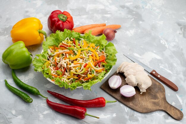 Вид сверху вкусный овощной салат с нарезанными овощами и целыми свежими овощами и сырыми куриными грудками на сером, салатная еда