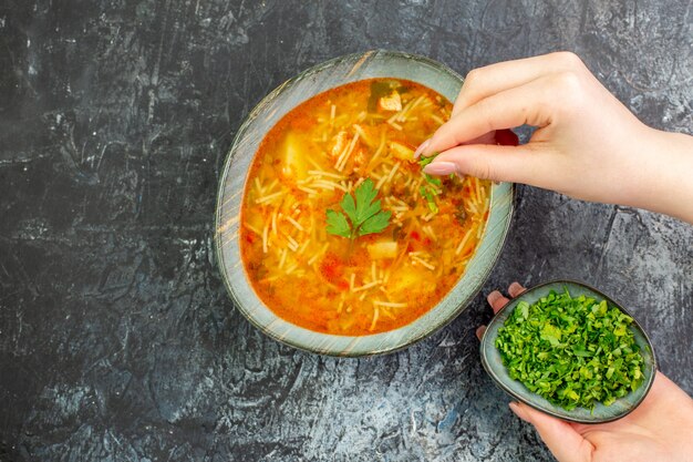 Вид сверху вкусный суп из вермишели внутри тарелки с зеленью на светло-сером столе