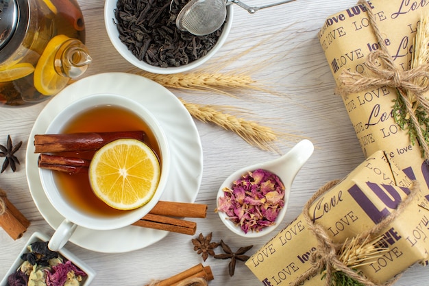 Vista dall'alto della pausa tè con cannella lime e limone in una tazza e una pentola intorno agli ingredienti necessari accanto ai regali su sfondo bianco