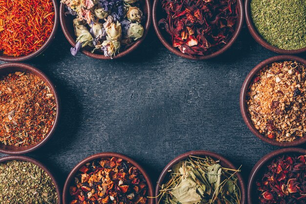 Top view tea herbs in bowls on dark textured background. horizontal space for text