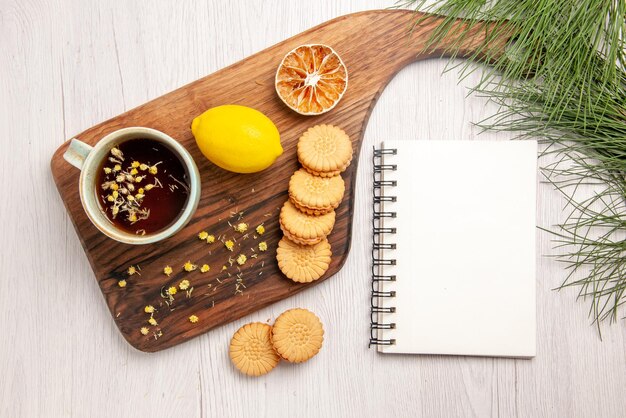 トップビューのお茶とレモンキッチンボードの白いノートとクリスマスツリーの枝にハーブクッキーとレモンとお茶を一杯