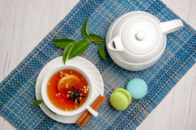 Top view tea with lemon white cup of tea with lemon cinnamon next to teapot French macaroons and leaves on the blue-white tablecloth