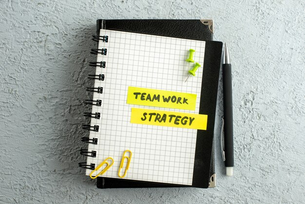 Top view of TEAMWORK STRATEGY writings on coloured sheets on spiral notebook and book on gray sand background