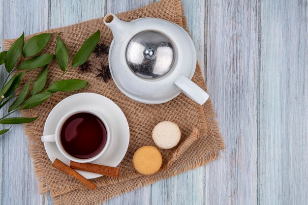 Чайник, вид сверху, чашка чая с корицей и миндальным печеньем на бежевой салфетке на сером столе