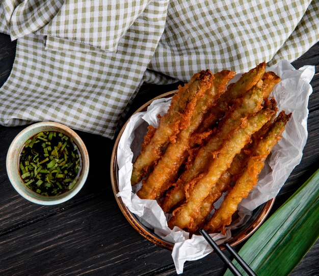 Top view of tempura vegetables in a bowl served with soy sauce on wood with plaid fabric