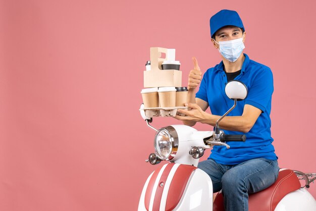 Top view of thankful male delivery person in mask wearing hat sitting on scooter delivering orders making ok gesture on peach