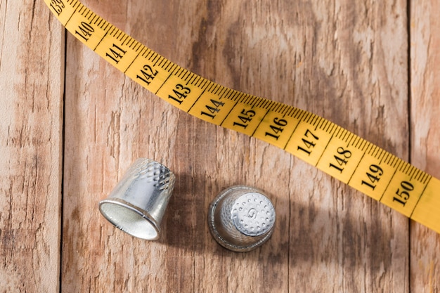 Top view of thimbles with measuring tape on wooden surface