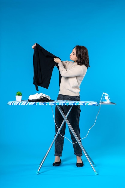 Top view of thinking young girl standing behind the iron board touching cloth on blue wave background