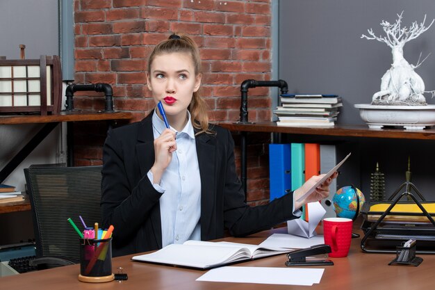 Top view of thinking young woman sitting at a table and holding a document in the office