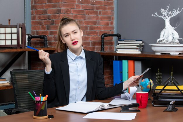 Top view of thoughtful woman sitting at a table and holding a document blue color pen in the office