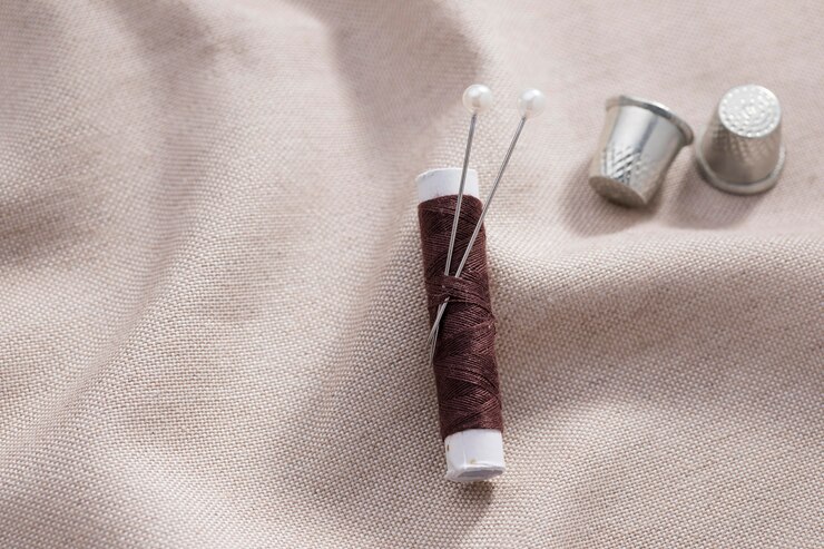 Free Photo top view of thread reel with needles and thimbles on textile