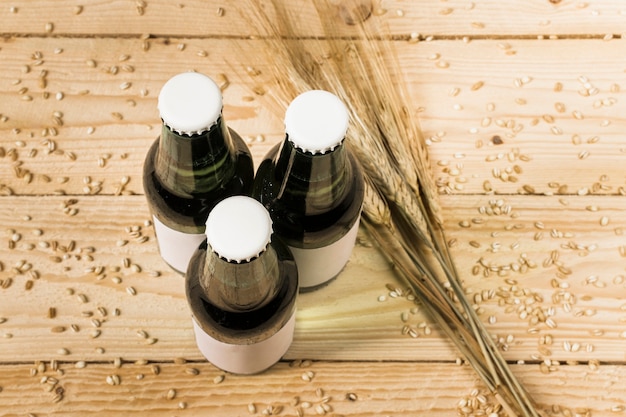 Free photo top view of three closed beer bottles and ears of wheat on wooden background