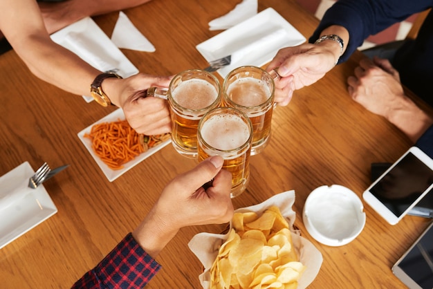 Top view of three unrecognizable friends toasting with beer mugs