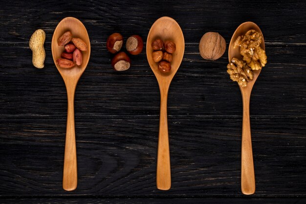 Top view three wooden spoons with hazelnuts peanuts and walnuts peeled and in shell