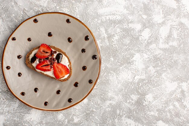 Top view of toast with strawberry and sour cream inside brown plate on the grey light surface