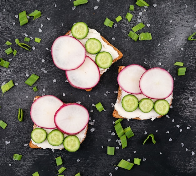 Free photo top view of toasts with radish and cucumber on black surface horizontal