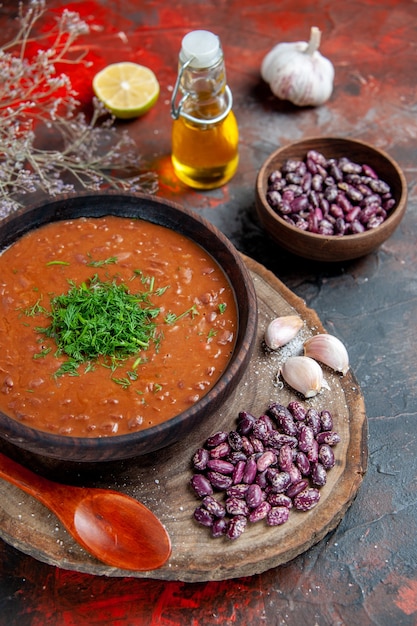 Top view of tomato soup beans garlic on wooden cutting board and oil bottle on mix color table