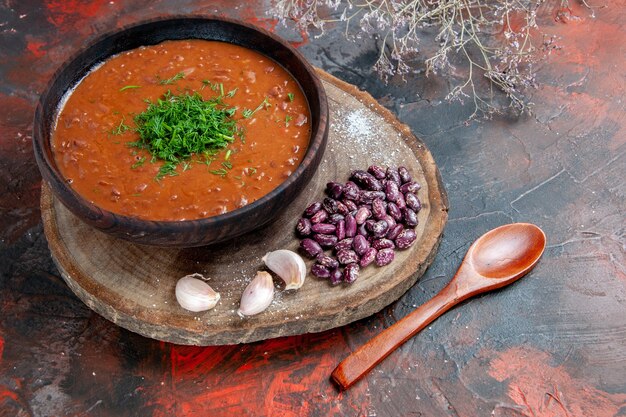 Вид сверху томатного супа с фасолью и чесноком на деревянной разделочной доске и ложкой на цветном фоне