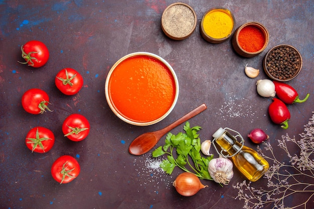 Vista dall'alto della zuppa di pomodoro cucinata con pomodori freschi con condimenti sul tavolo nero