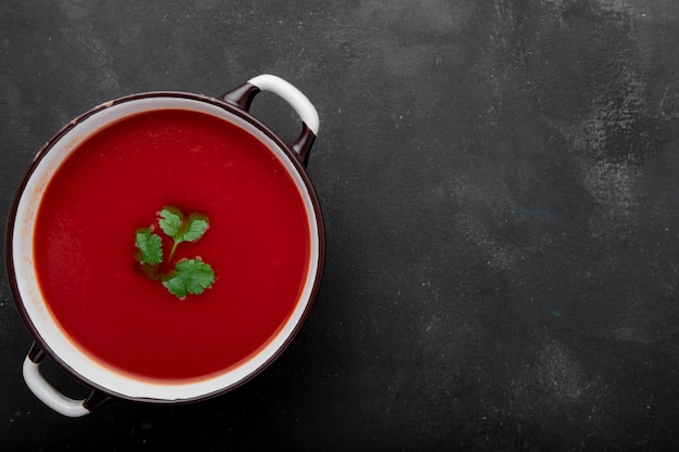 Top view of tomato soup on left side on black surface